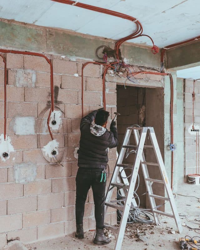 An electrician running wiring on a building site, working from a stepladder
